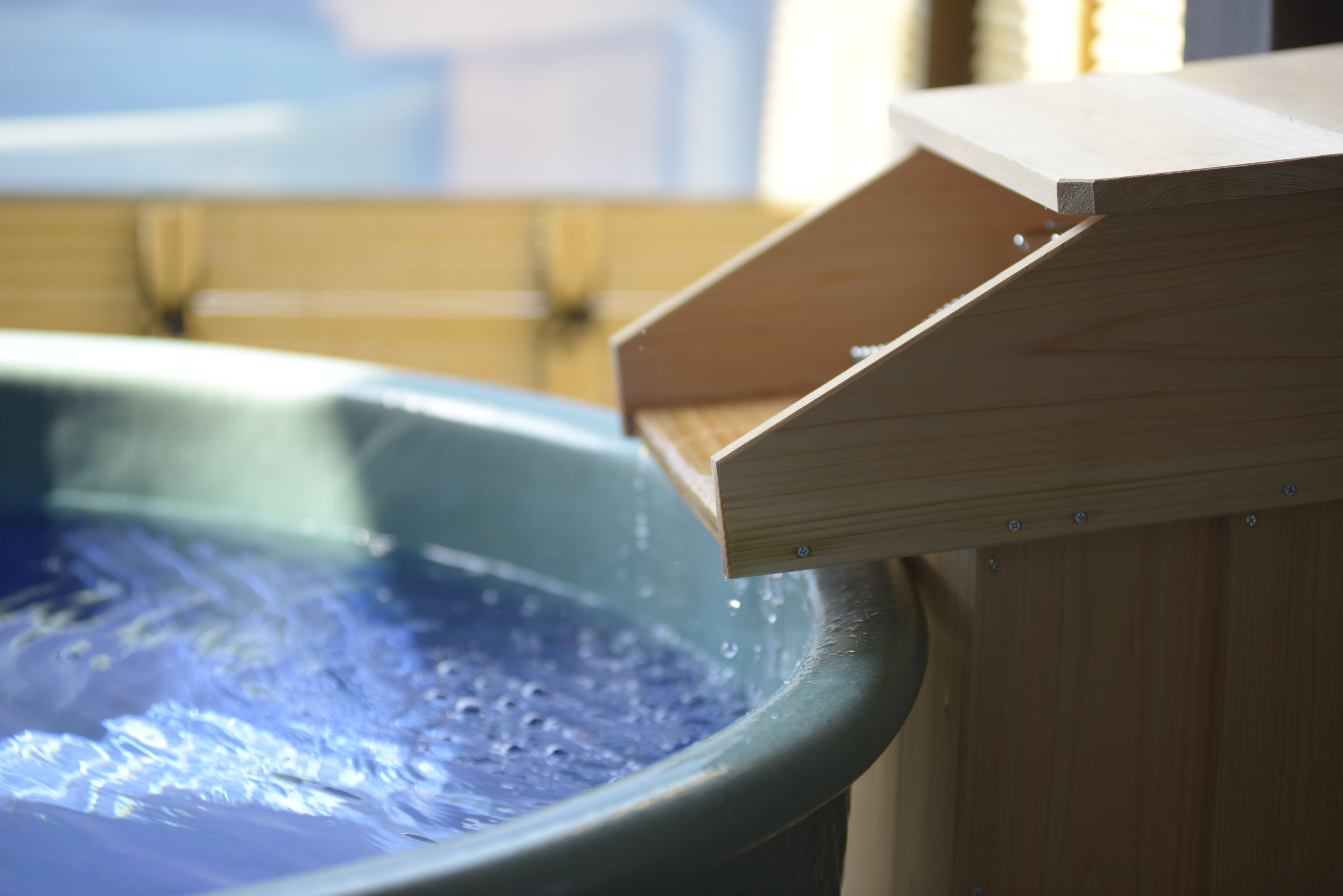 A wooden structure with a slanted roof, possibly a deck or a part of a building, adjacent to a large, round, blue water feature.
