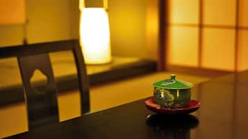 Een tafel met een groene kom op een rode schotel, een zwarte stoel en een brandende lamp op de achtergrond.