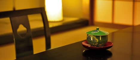 A table with a green bowl on a red saucer, a black chair, and a lit lamp in the background.