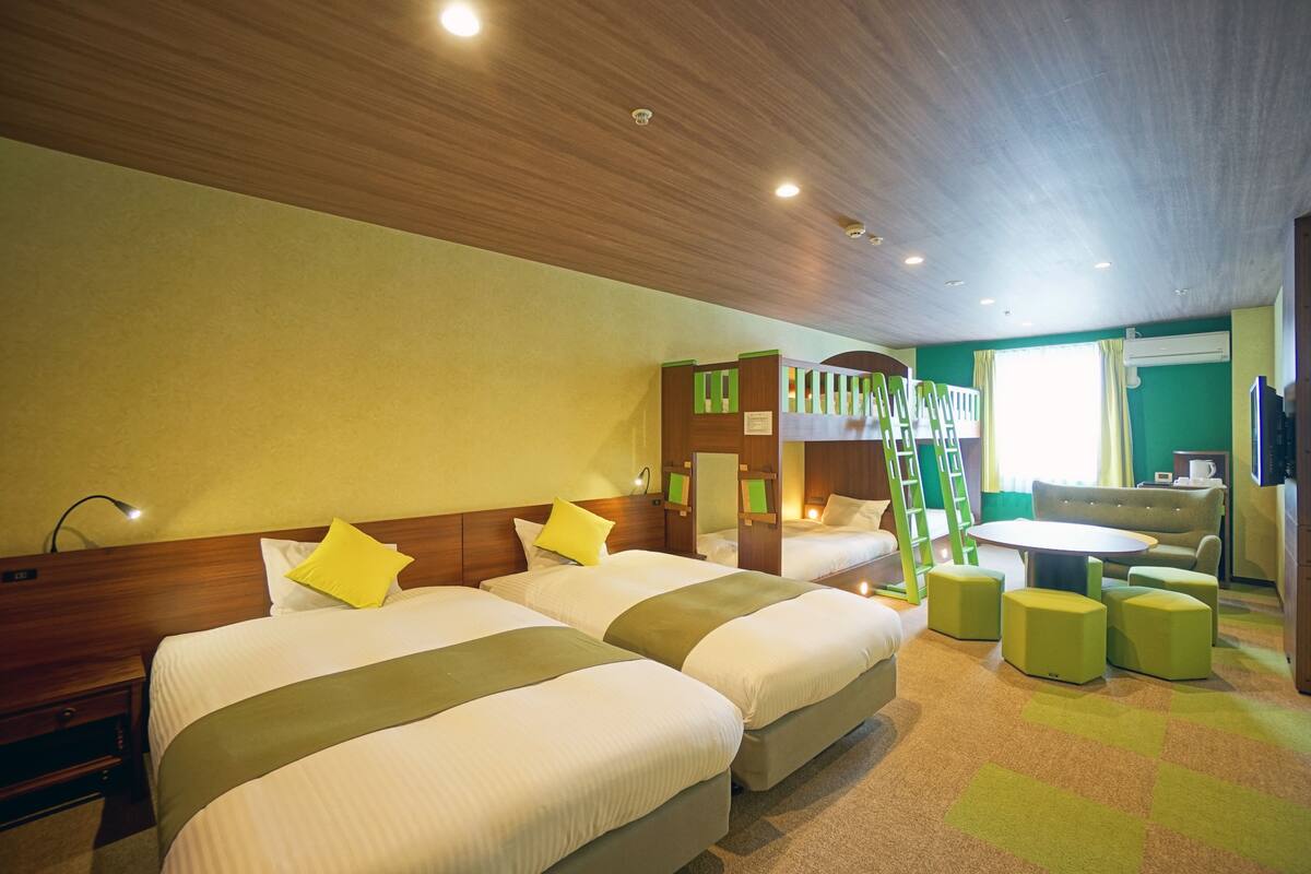 A hotel room with two beds, a green sofa, a round table, and a ladder.