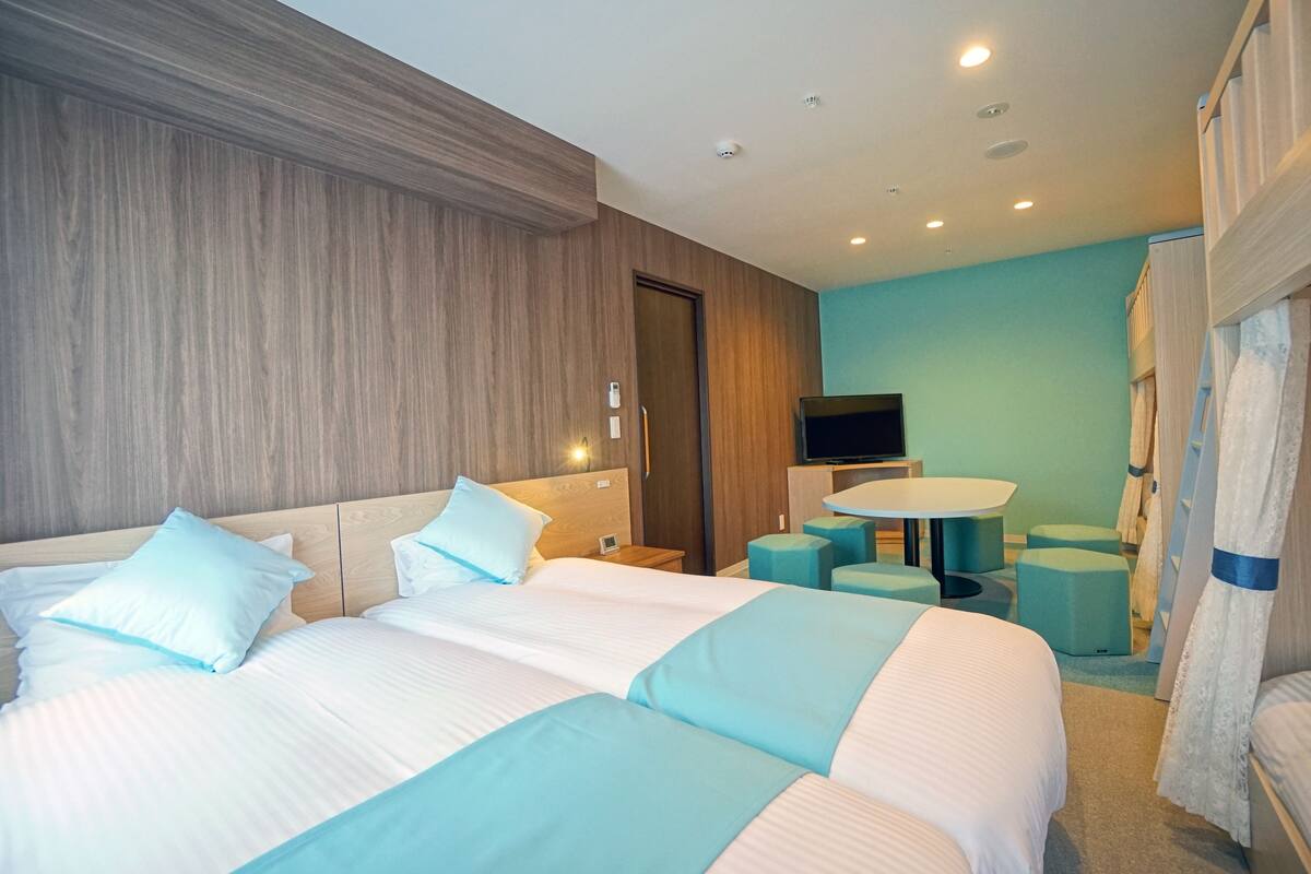 A hotel room with two beds, a TV, a small table, and a seating area.