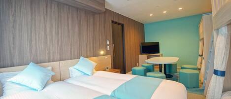 A hotel room with two beds, a TV, a small table, and a seating area.