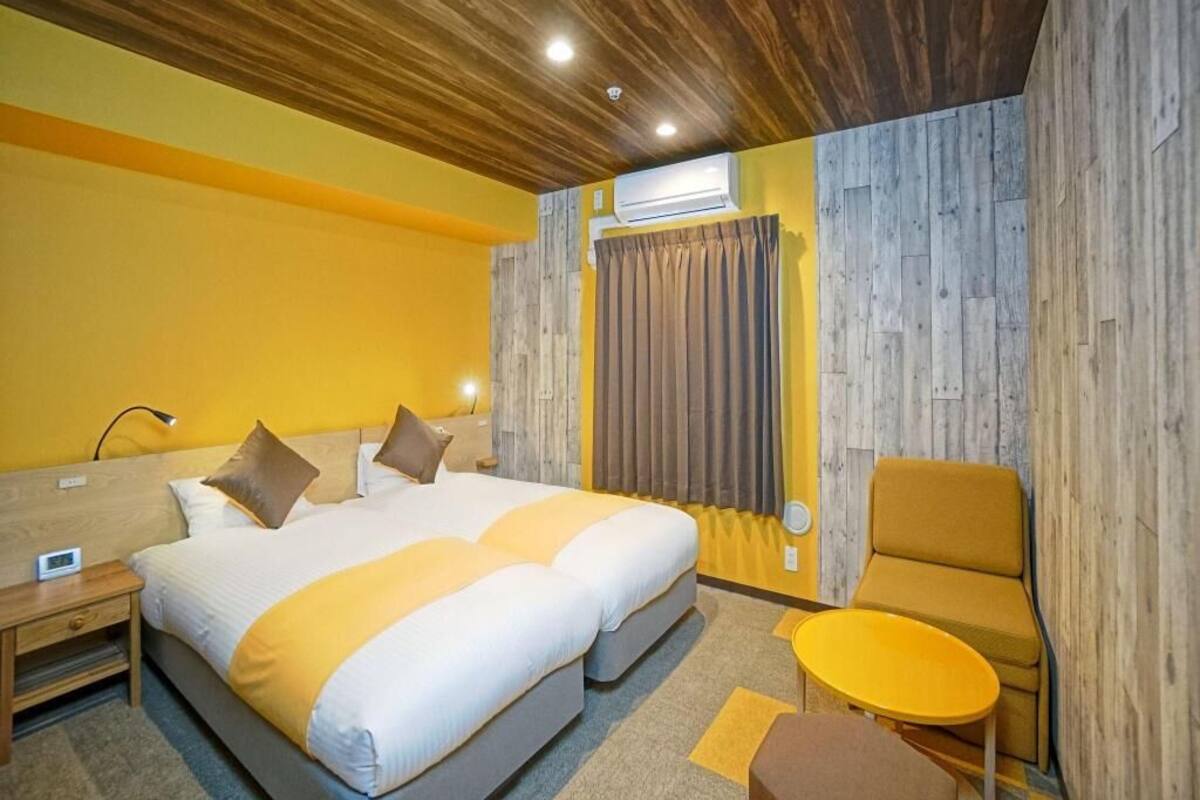 A hotel room with a wooden ceiling, a bed with two pillows, a small round table, and a chair.