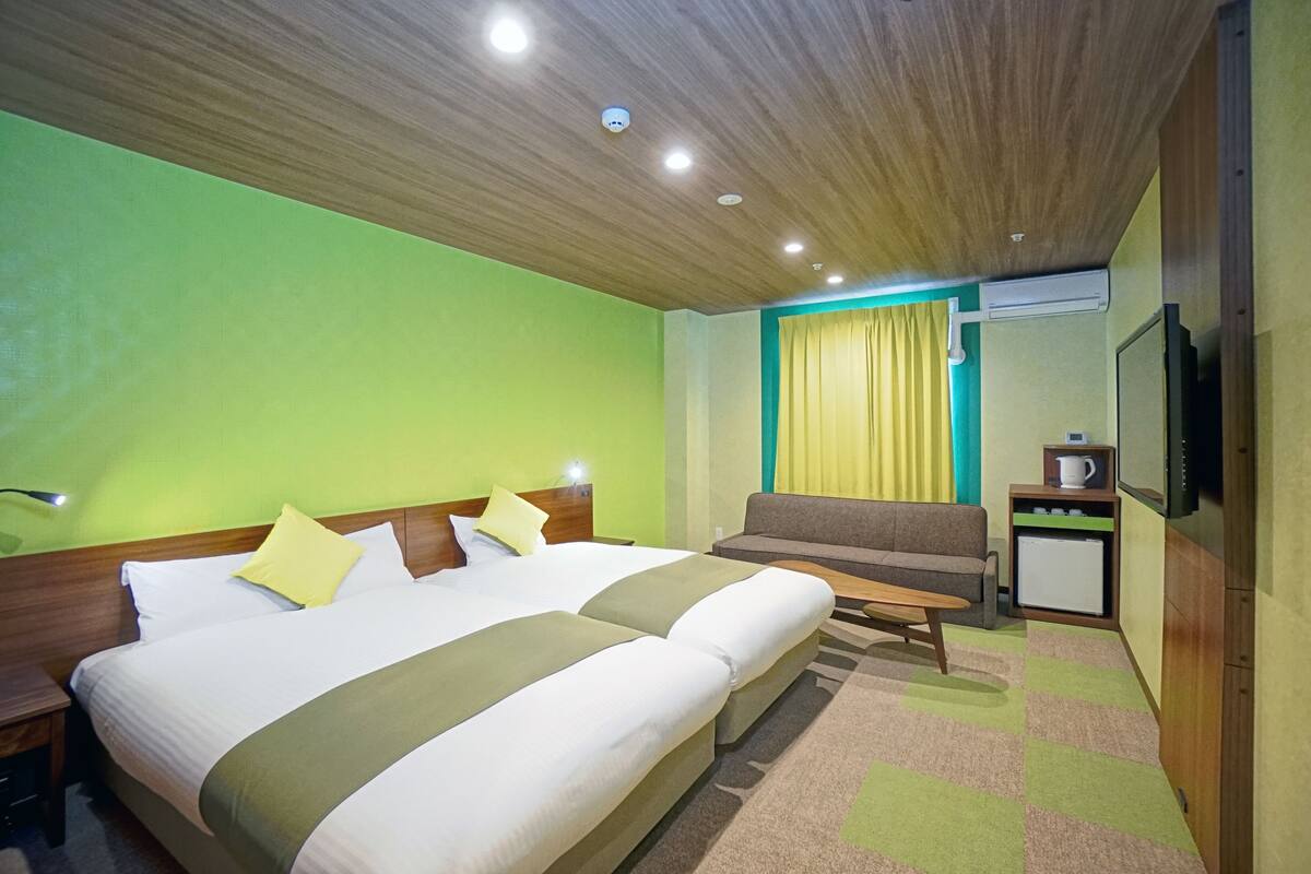 A hotel room with a large bed, a sofa, a small table, and a TV.