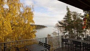 A deck with outdoor seating overlooking a lake, surrounded by trees with autumn foliage. - Äijälän Rusti Paratiisisaari (Naantali)