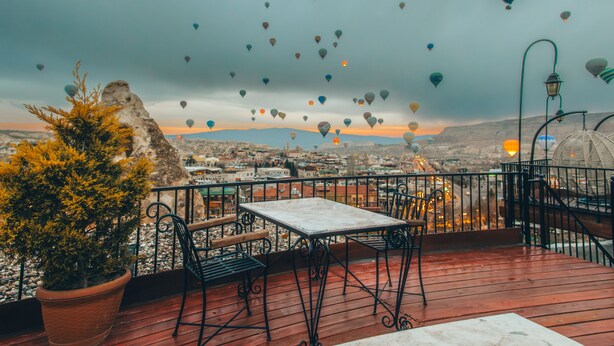 A terrace with a table and chairs, overlooking a cityscape with hot air balloons in the sky. - Bedrock Cave Hotel - Adults Only (Nevsehir)