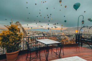 Una terraza con mesa y sillas, con vistas a un paisaje urbano donde se ven globos aerostáticos en el cielo.
