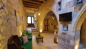 A cozy interior with a stone fireplace, wooden furniture, and a television mounted on the wall. - Bedrock Cave Hotel - Adults Only (Nevsehir)