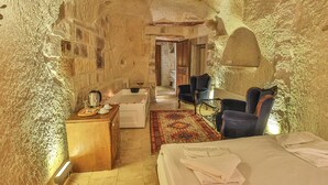 A room with a stone wall, a wooden dresser, a bed with towels, a chair, a table, and a bathtub. - Bedrock Cave Hotel - Adults Only (Nevsehir)