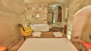 A stone-walled room with a bed, a yellow armchair, a bathtub, and a small table with a red cushion. - Bedrock Cave Hotel - Adults Only (Nevsehir)
