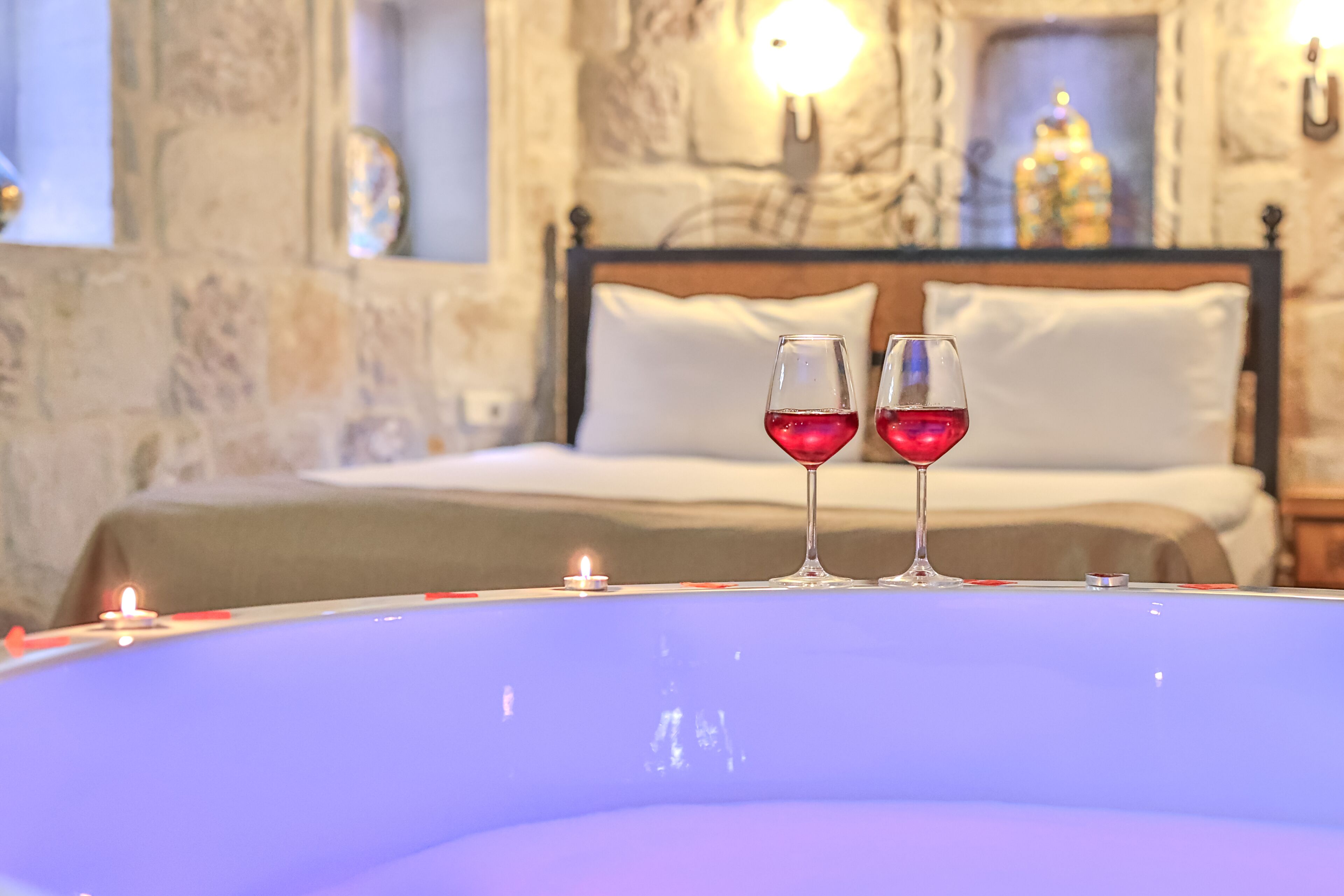 A room with a bed, two wine glasses on a table, and a lit candle.