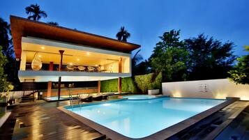 A modern two-story house with a swimming pool, outdoor seating, and a well-lit patio area.