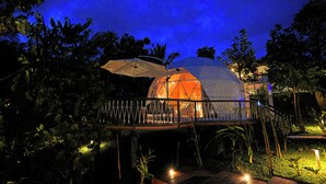 A dome-shaped structure with a wooden deck and railing, surrounded by lush vegetation.