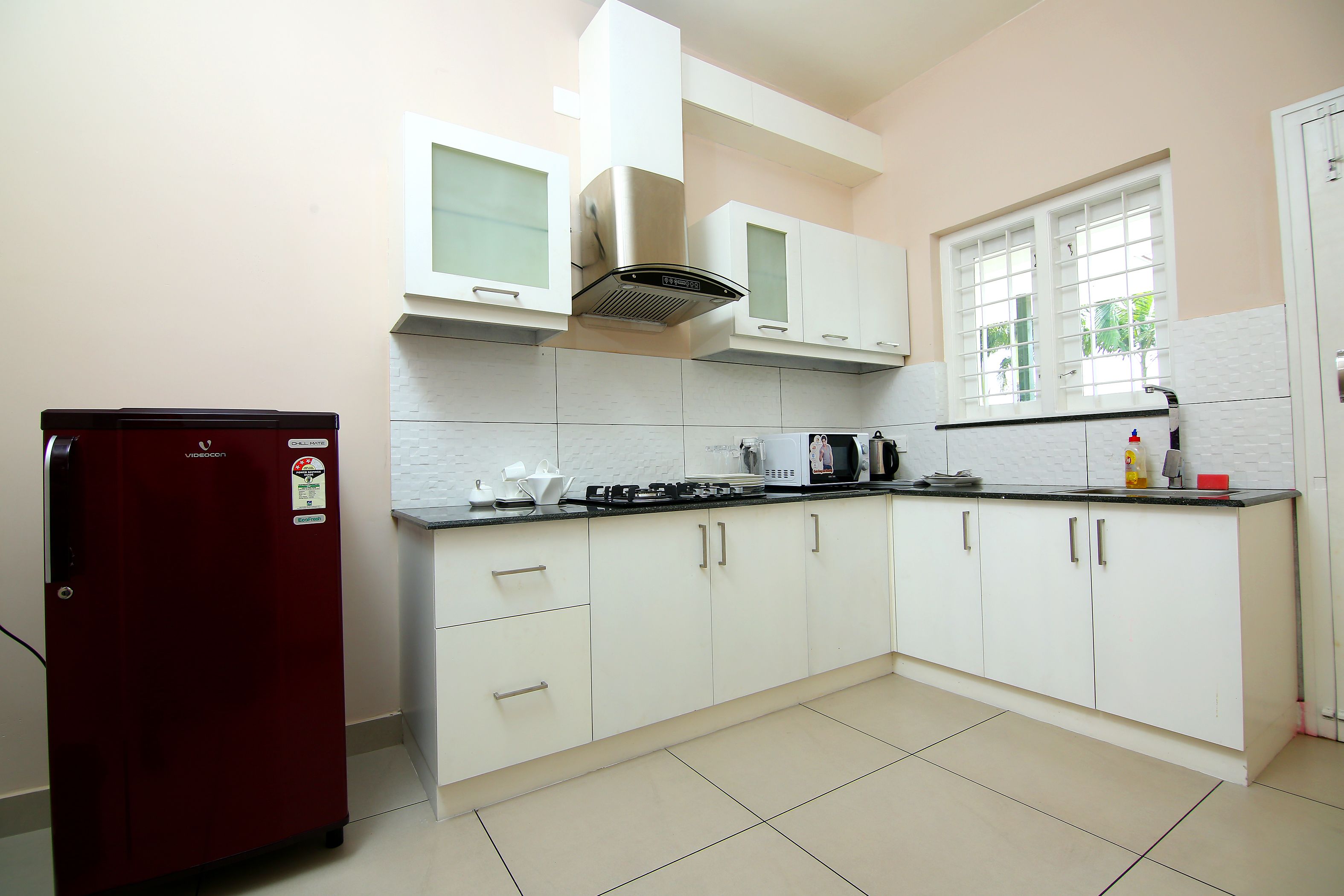 A kitchen with white cabinets, a red refrigerator, and a window with blinds.
