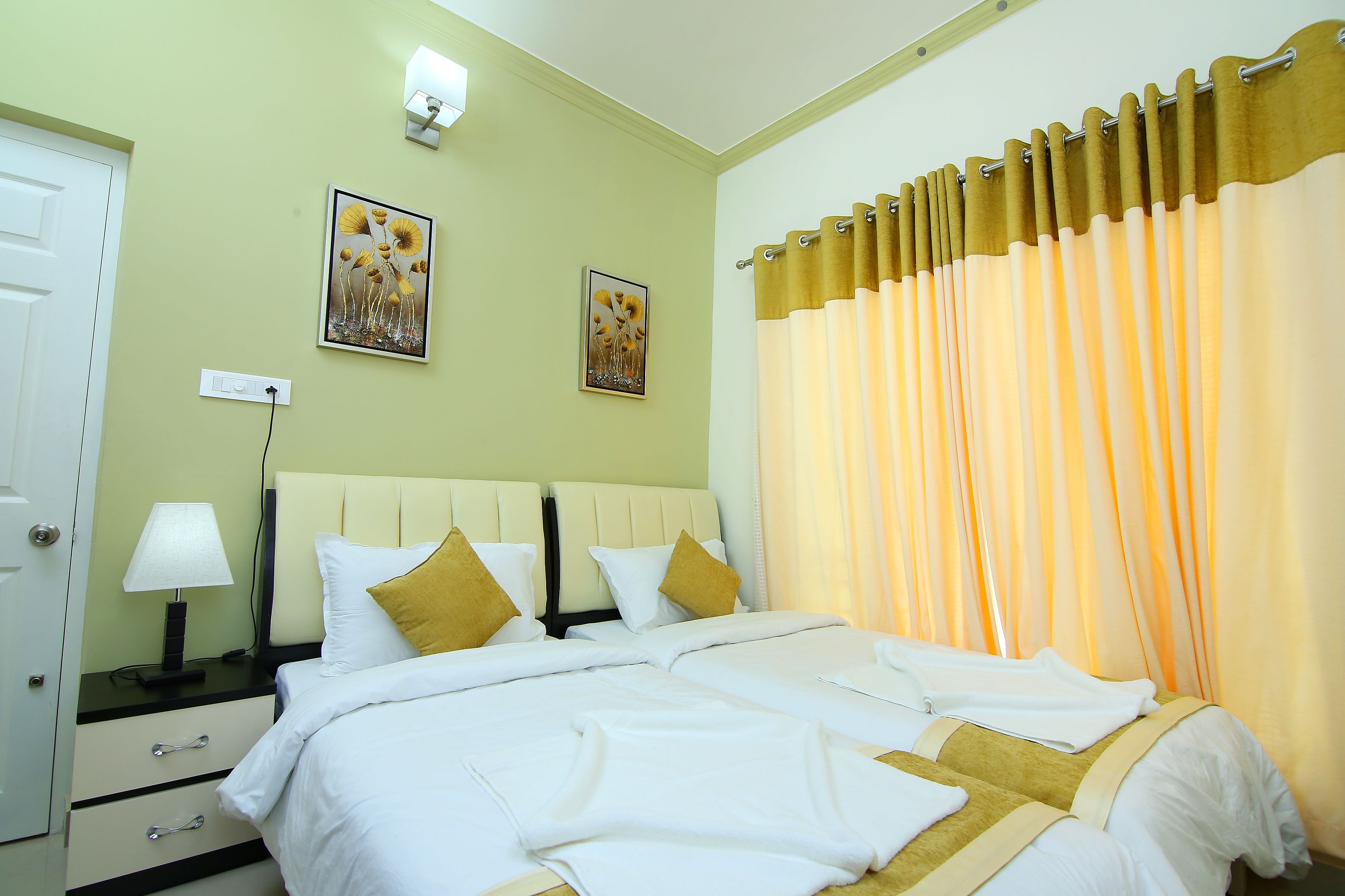 A neatly made bed with white linens and two pillows, a bedside table with a lamp, and two wall-mounted paintings.