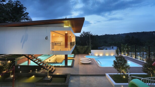 A modern house with a swimming pool, outdoor seating, and a well-lit entrance.