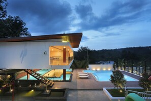 Una casa moderna con piscina, mobiliario de exterior e ingreso bien iluminado.