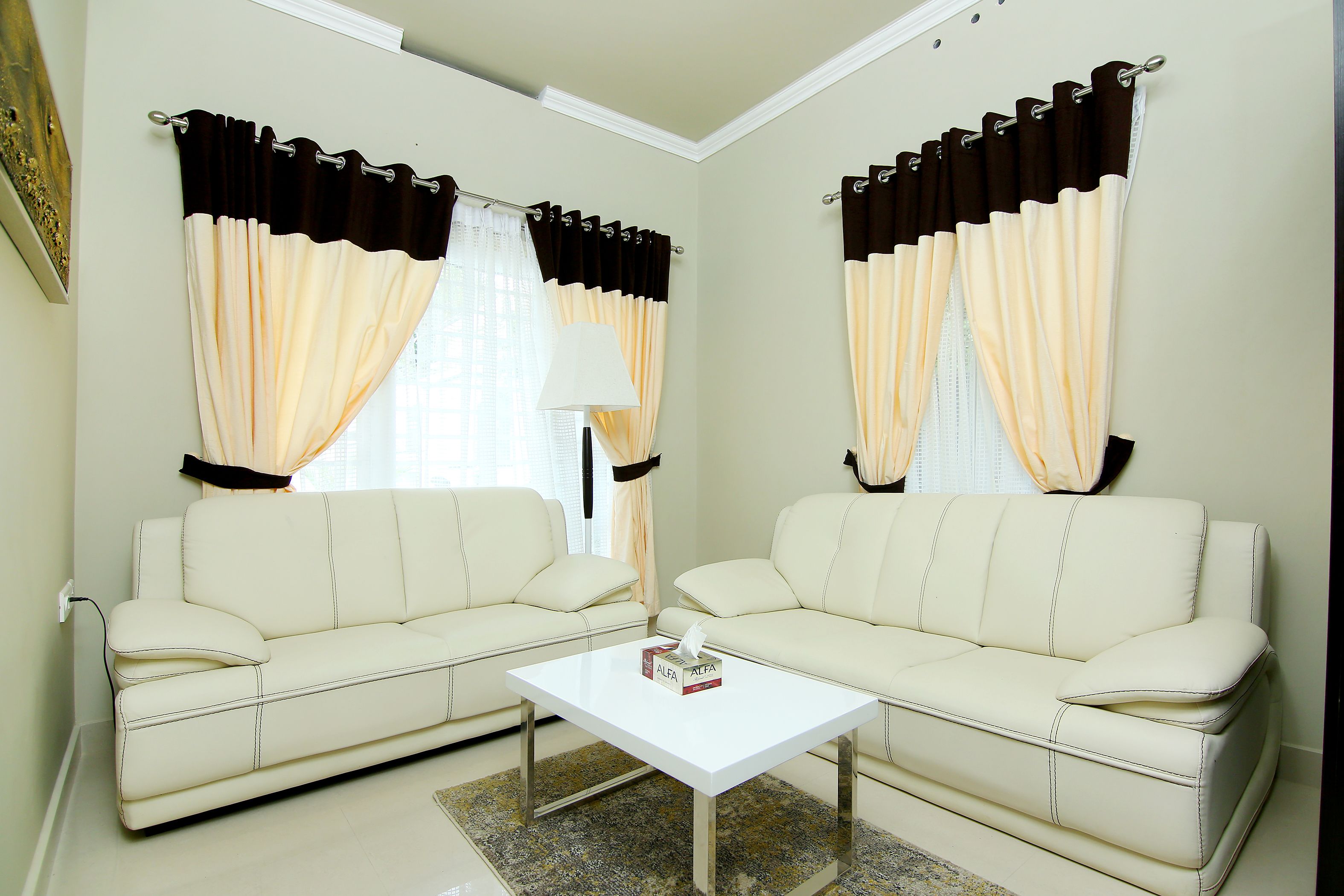 A living room with two cream-colored sofas, a white coffee table, and curtains with a black and cream pattern.