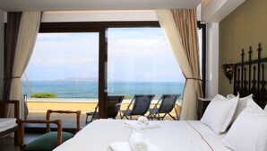 A hotel room with a bed, a chair, a table, and a view of the sea. - Kouvohori Villas Crete (Hersonissos)