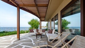 A covered outdoor seating area with a view of the sea, furnished with wooden chairs and sofas, and a small table. - Kouvohori Villas Crete (Hersonissos)