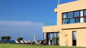 A modern building with a glass balcony overlooking the sea, equipped with sun loungers and umbrellas. - Kouvohori Villas Crete (Hersonissos)