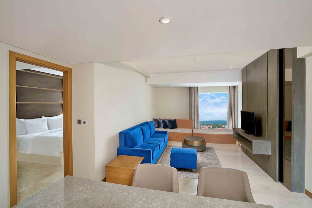 Ett modernt hotellrum med en stor säng, en blå soffa, en TV och utsikt över stranden.