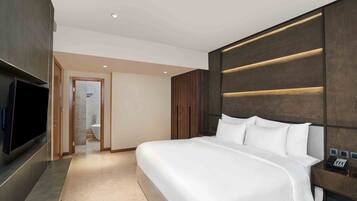 A modern hotel room with a large bed, a flat-screen TV, a bedside telephone, and a bathroom visible through an open door.