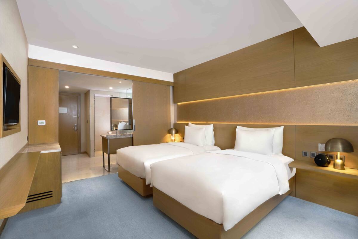 Ett modernt hotellrum med två sängar, ett skrivbord och ett badrum som syns genom en öppen dörr.