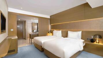 A modern hotel room with two beds, a desk, and a bathroom visible through an open door.
