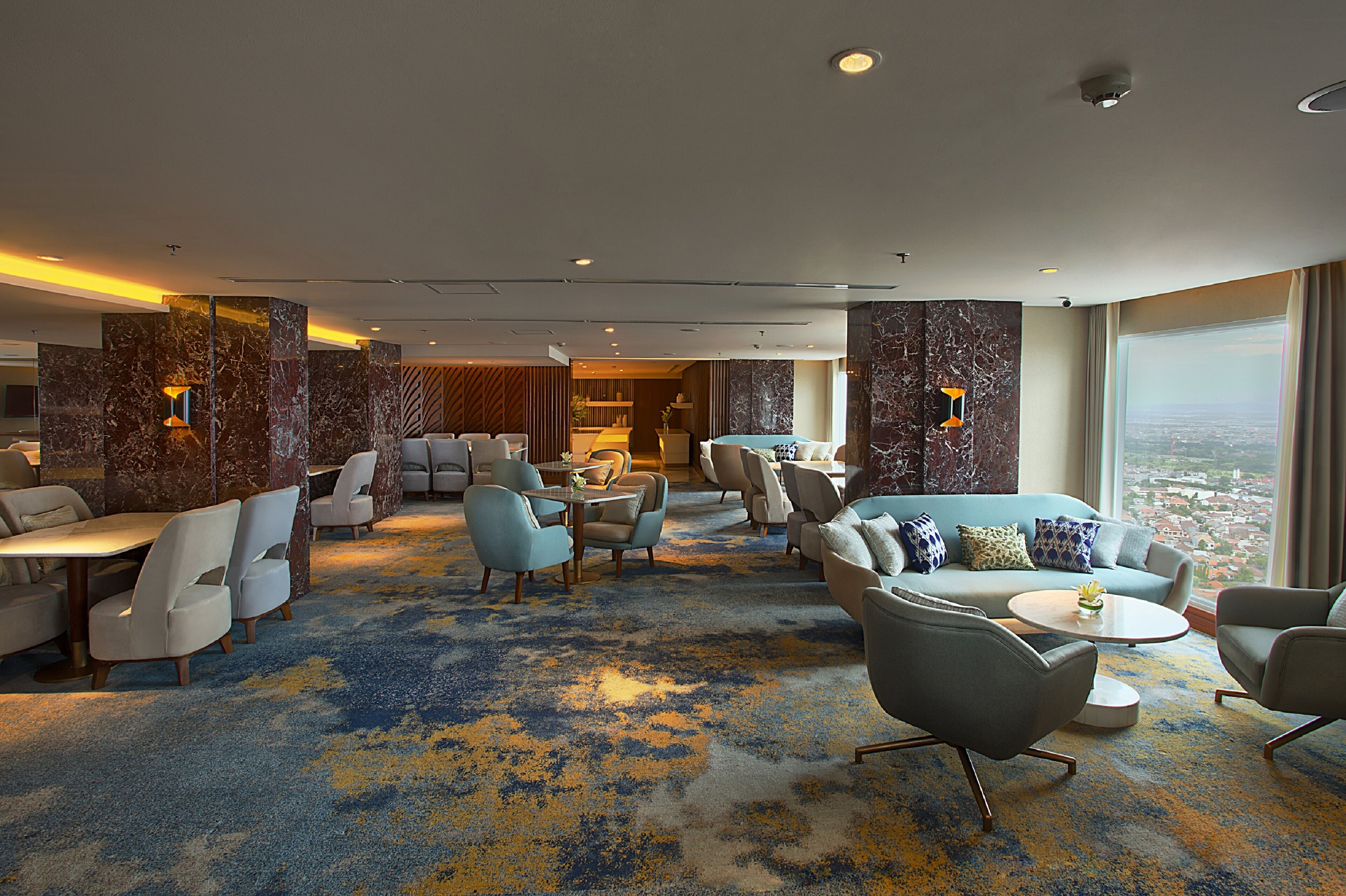 A spacious hotel lobby with a marble reception desk, multiple seating areas, and a large window offering a city view.