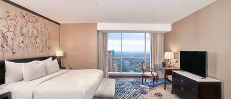 Habitación de hotel con una cama grande, un escritorio con televisión y vistas a la ciudad a través de amplios ventanales.