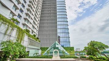 Un immeuble moderne de grande hauteur, doté d’une façade en verre, entouré d’une végétation luxuriante et surplombant un ciel dégagé.