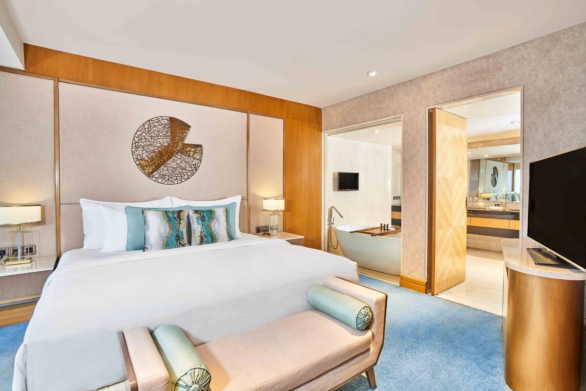 Ett modernt hotellrum med en stor säng, en sittgrupp, en TV och ett badrum som syns genom en öppen dörr.