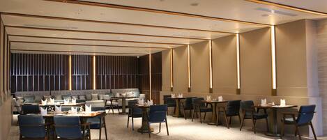 A modern hotel lobby with a seating area, tables, and a bar.