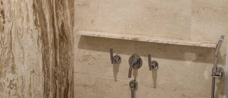 A bathroom with a shower, marble walls, and a metal shelf.