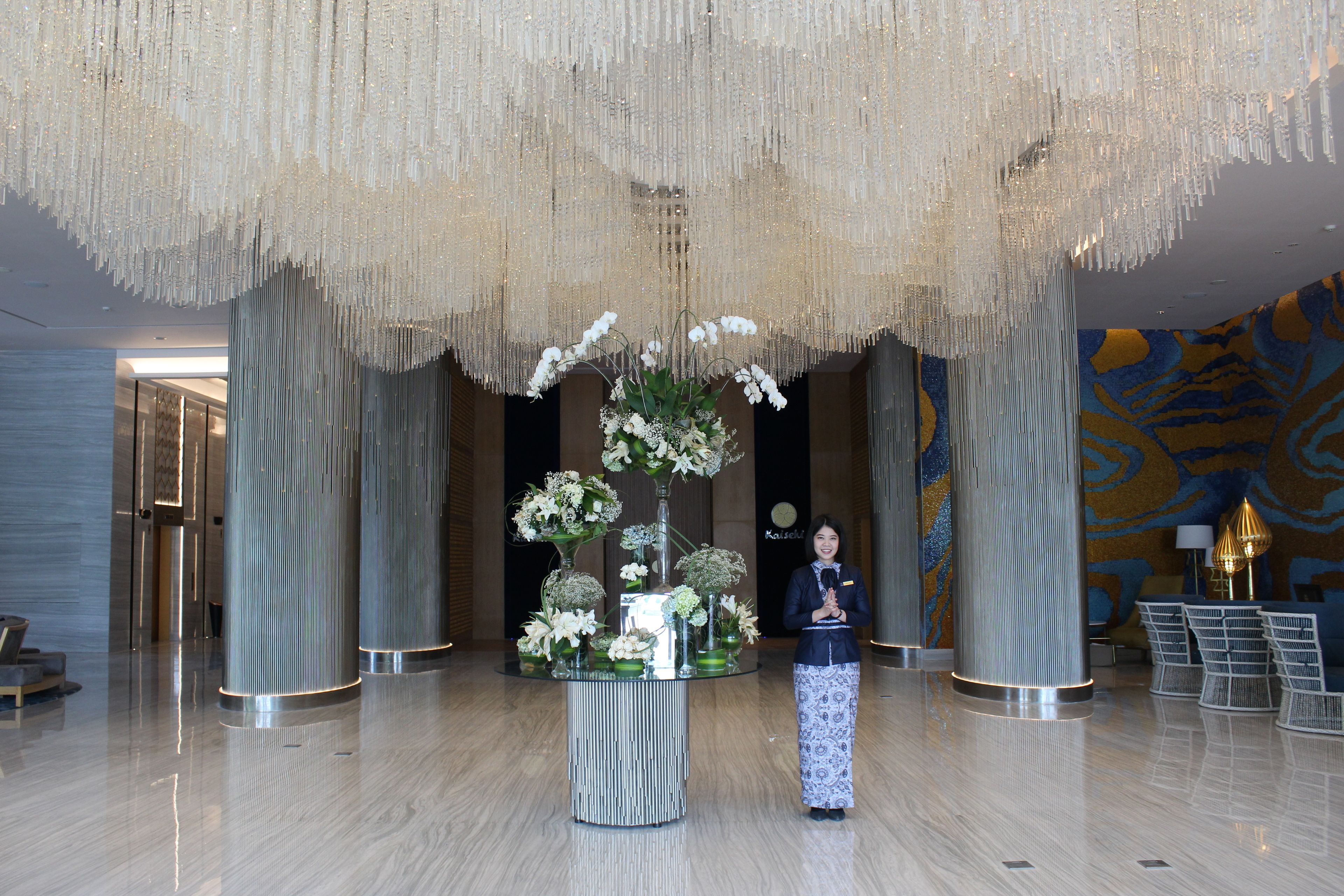 A lobby with a central floral arrangement on a glass table, surrounded by seating.