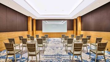 A conference room with a large screen at the front, rows of chairs, and a patterned carpet.
