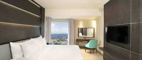 A modern hotel room with a large bed, a desk, a chair, a TV, and a city view.