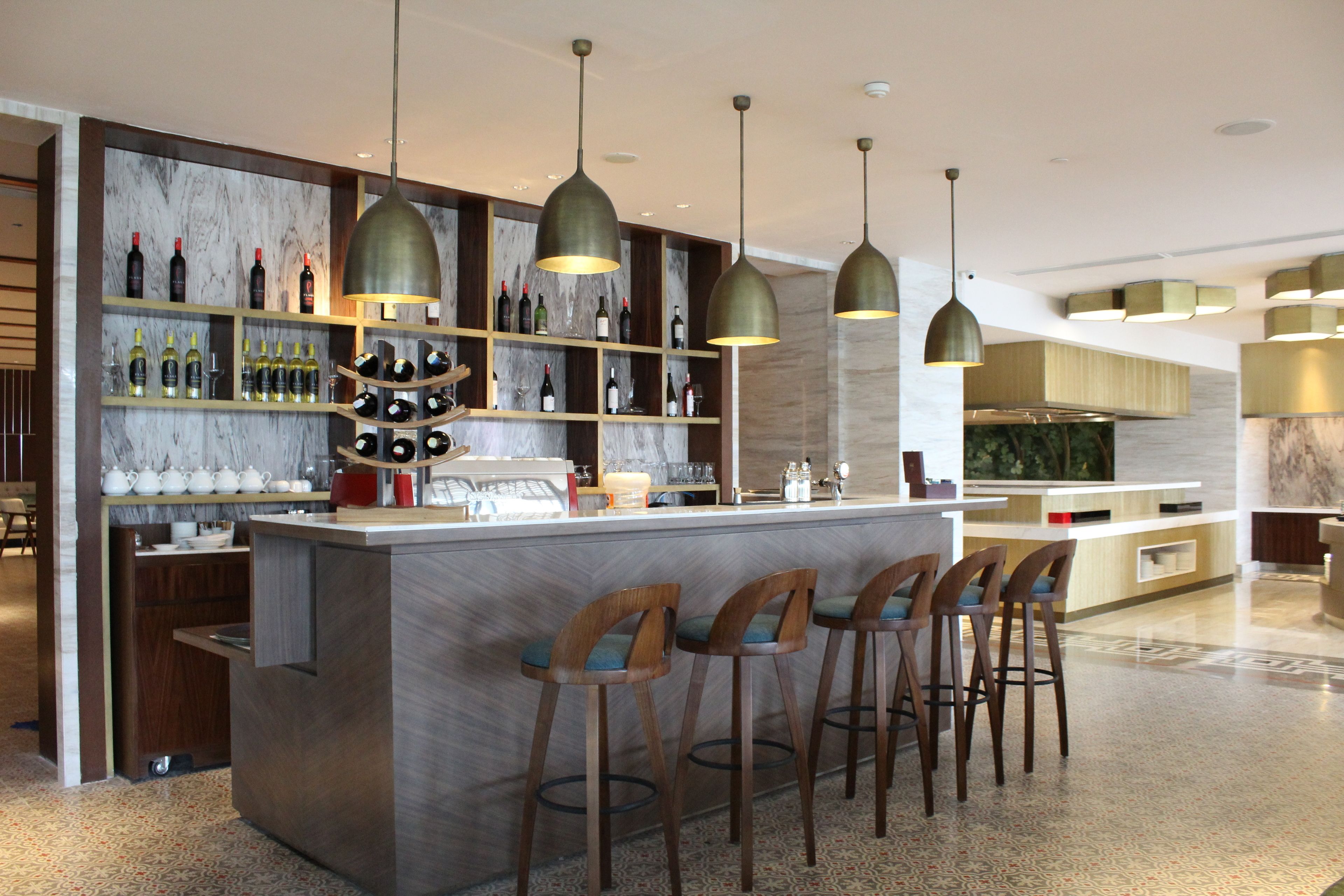 A modern bar area with a marble backsplash, wooden shelves with bottles, and pendant lighting.