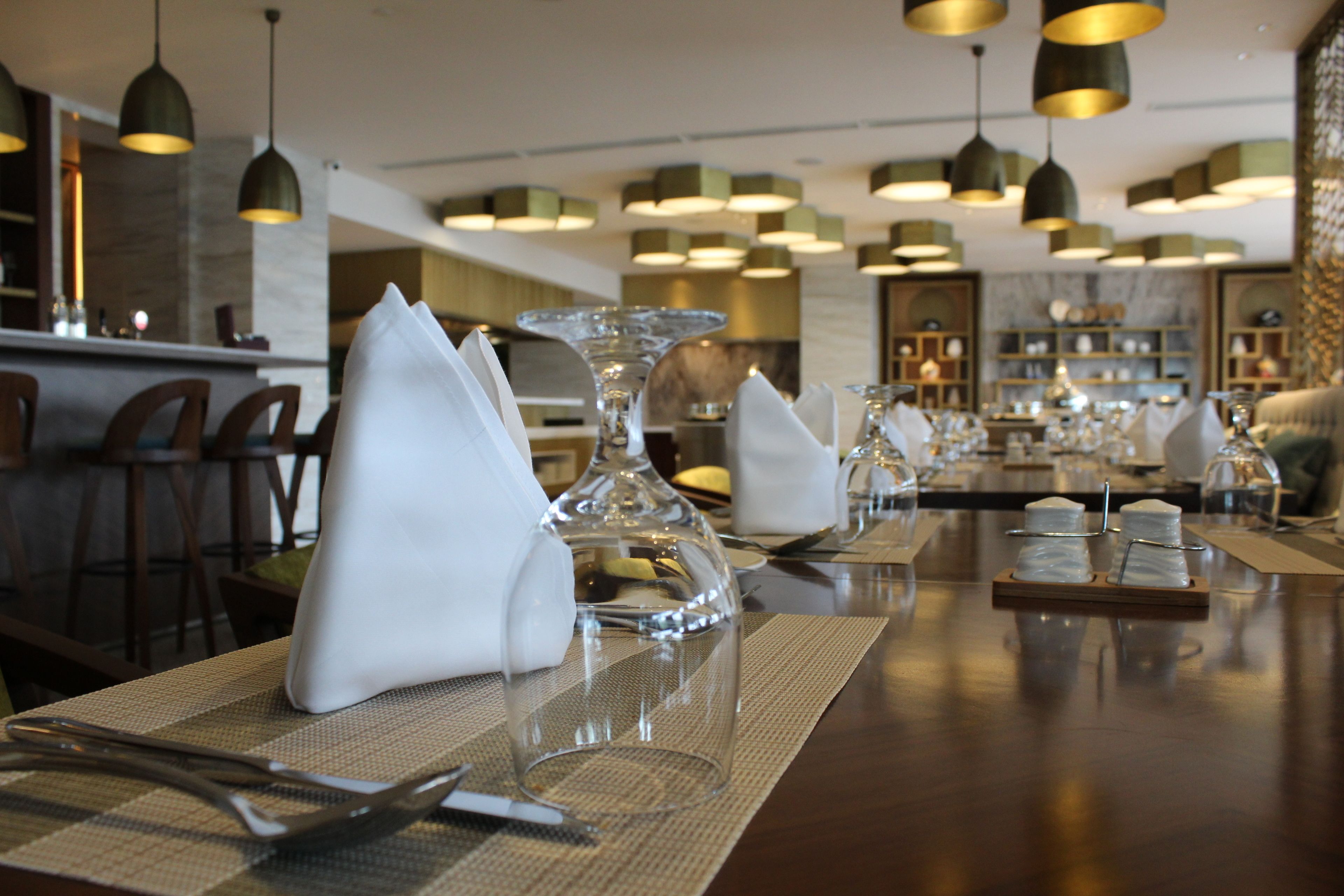 A restaurant with multiple tables set with white napkins, clear glassware, and a variety of dishes.