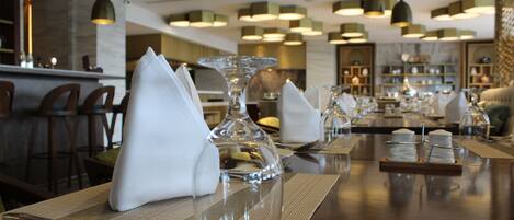Een restaurant met meerdere tafels, voorzien van witte servetten, glanzend servies en diverse gerechten.