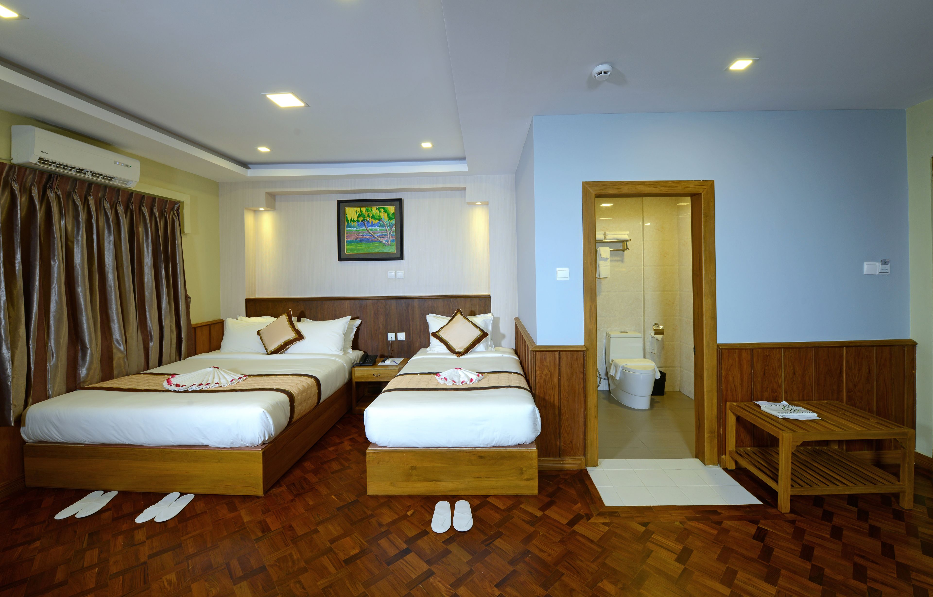 A hotel room with two beds, a wooden headboard, a painting on the wall, and a wooden table.