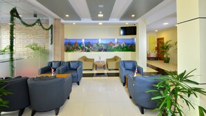A lobby with a seating area, a reception desk, a large wall mural, and potted plants. - Hotel H Valley Yangon (Yangon)