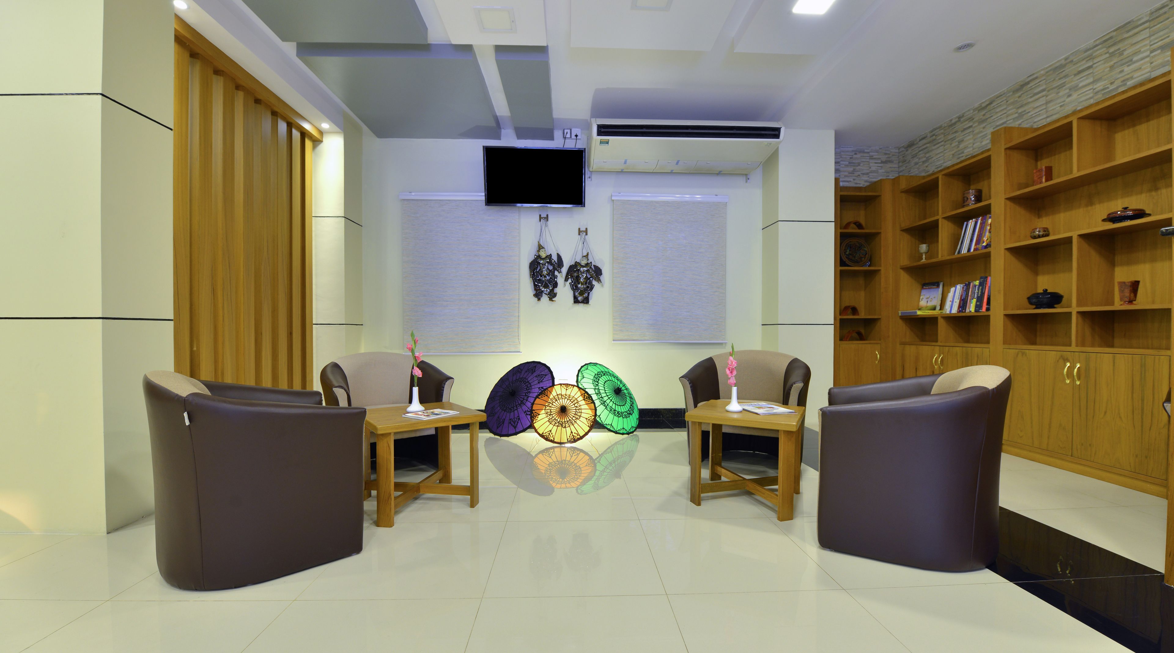 A modern waiting area with two sofas, a wooden table with umbrellas, a TV, and a bookshelf.
