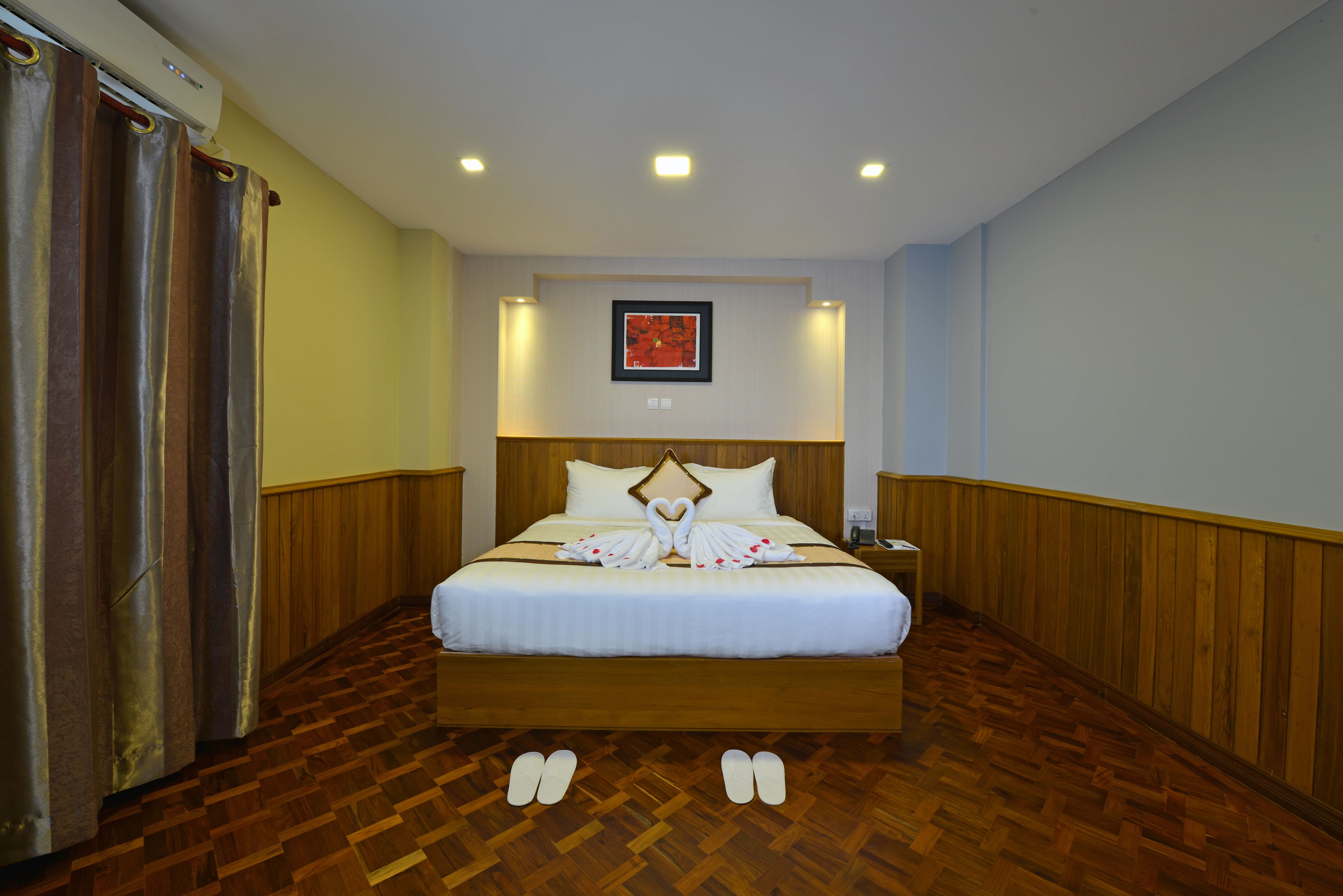 Habitación de hotel con una cama grande, paneles de madera, un cuadro en la pared y un par de pantuflas en el suelo.