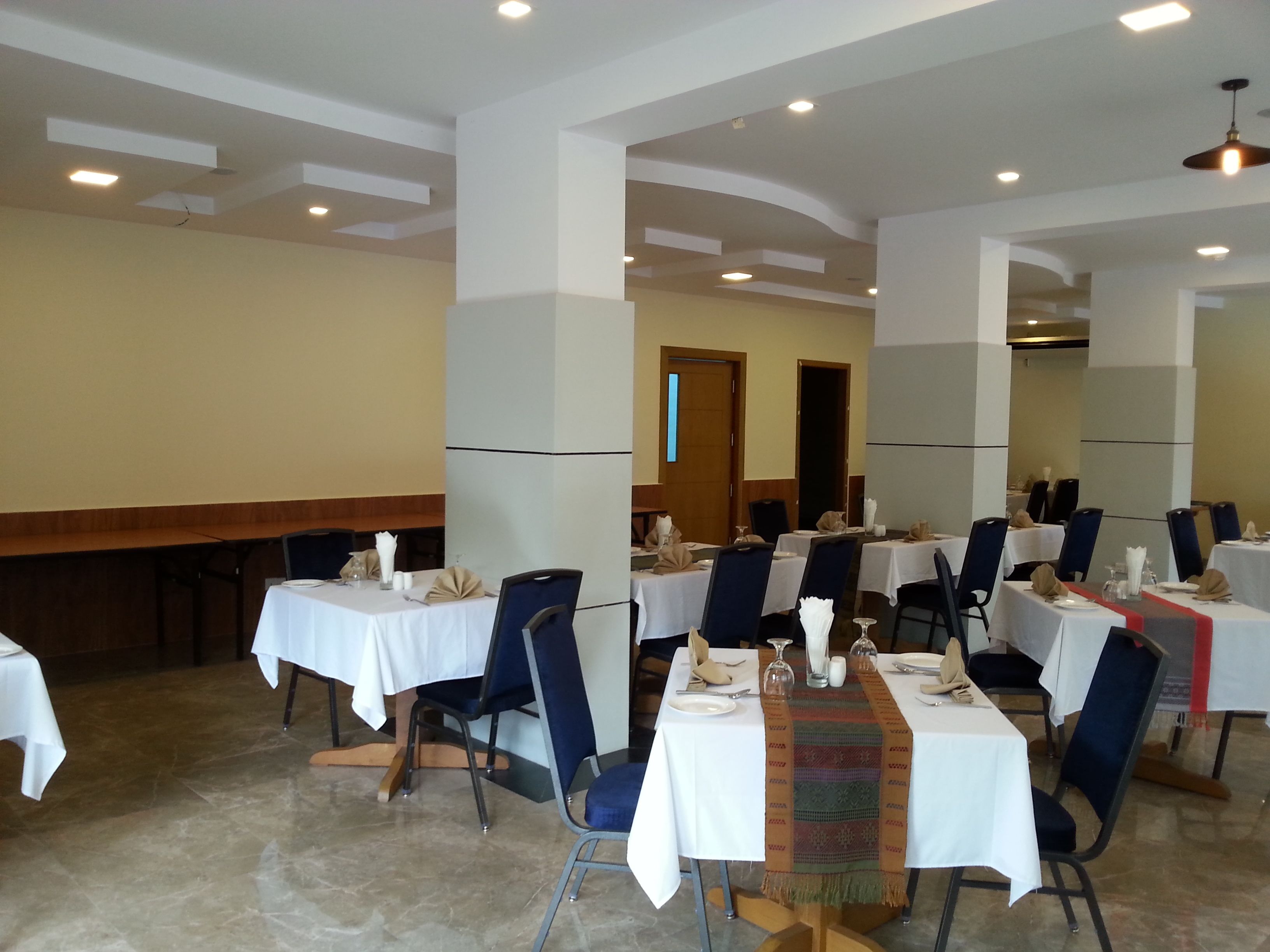 A dining area with tables set for four, each with white tablecloths, blue chairs, and neatly arranged cutlery.