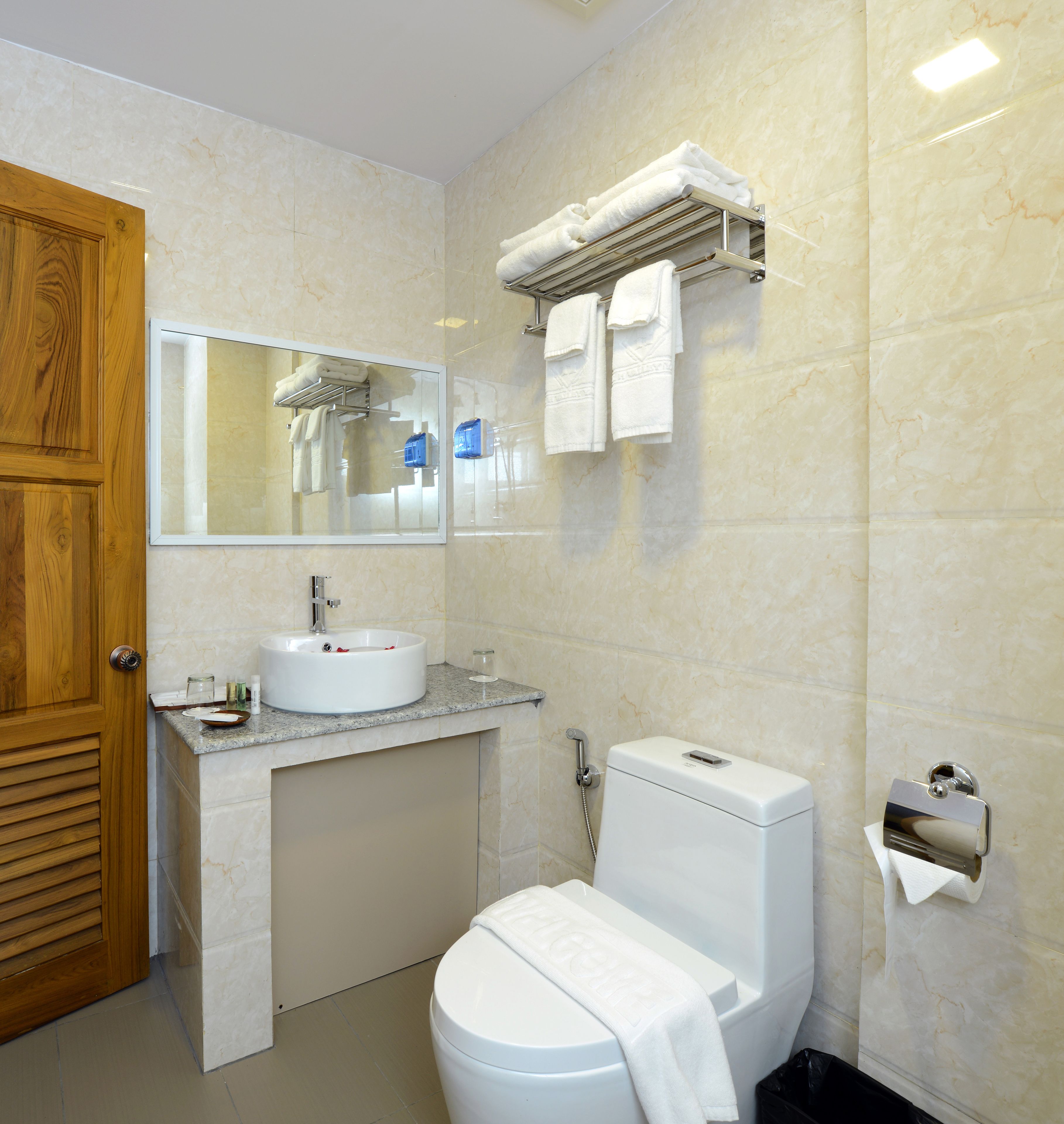 Un baño moderno con puerta de madera, un lavamanos blanco, un inodoro y un perchero para toallas.
