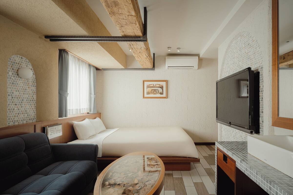 A modern hotel room with a bed, sofa, TV, and a coffee table.