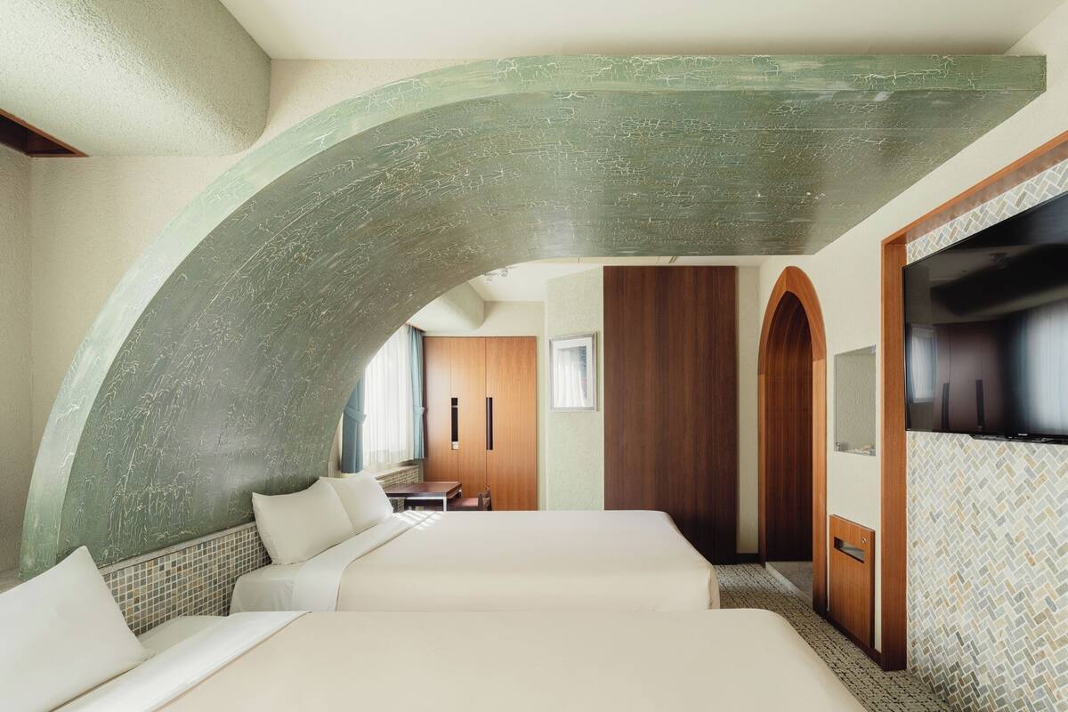 A hotel room with a curved green ceiling, a bed, a TV, and a wooden wardrobe.