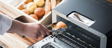 Eine Person legt mit einer Zange ein Brötchen in einen Toaster.